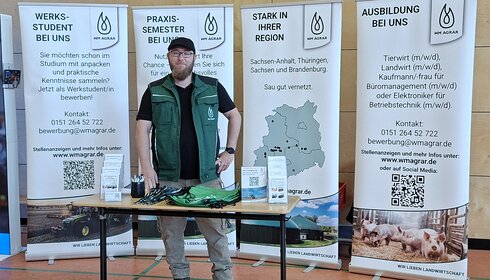 Mitarbeiter von WM Agrar an seinem Stand bei der Berufsorientierungsmesse in Rossla. Hinter ihm stehen vier Banner mit Informationen