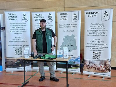 Mitarbeiter von WM Agrar an seinem Stand bei der Berufsorientierungsmesse in Rossla. Hinter ihm stehen vier Banner mit Informationen