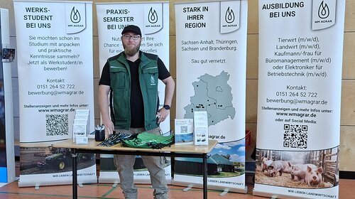 Mitarbeiter von WM Agrar an seinem Stand bei der Berufsorientierungsmesse in Rossla. Hinter ihm stehen vier Banner mit Informationen